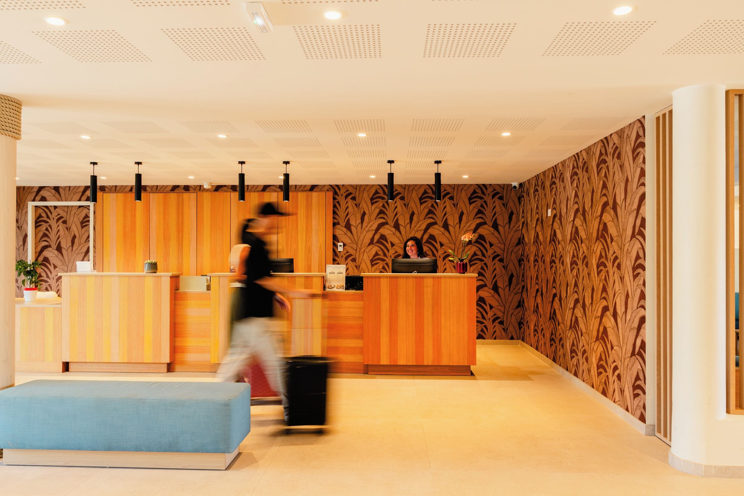 Un espace d’accueil avec un comptoir de réception en bois, un banc bleu et un mur orné de motifs.