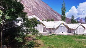 A series of white tents with prayer flags, set against a mountainous backdrop. - Himalayan Hideout (Leh)