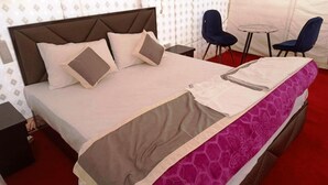 A neatly made bed with a headboard, two pillows, and a blanket. There are two chairs and a small round table in the room. - Himalayan Hideout (Leh)