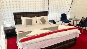 A hotel room with a large bed, a bedside table, a chair, a small table, and a tent-like structure in the background. - Himalayan Hideout (Leh)