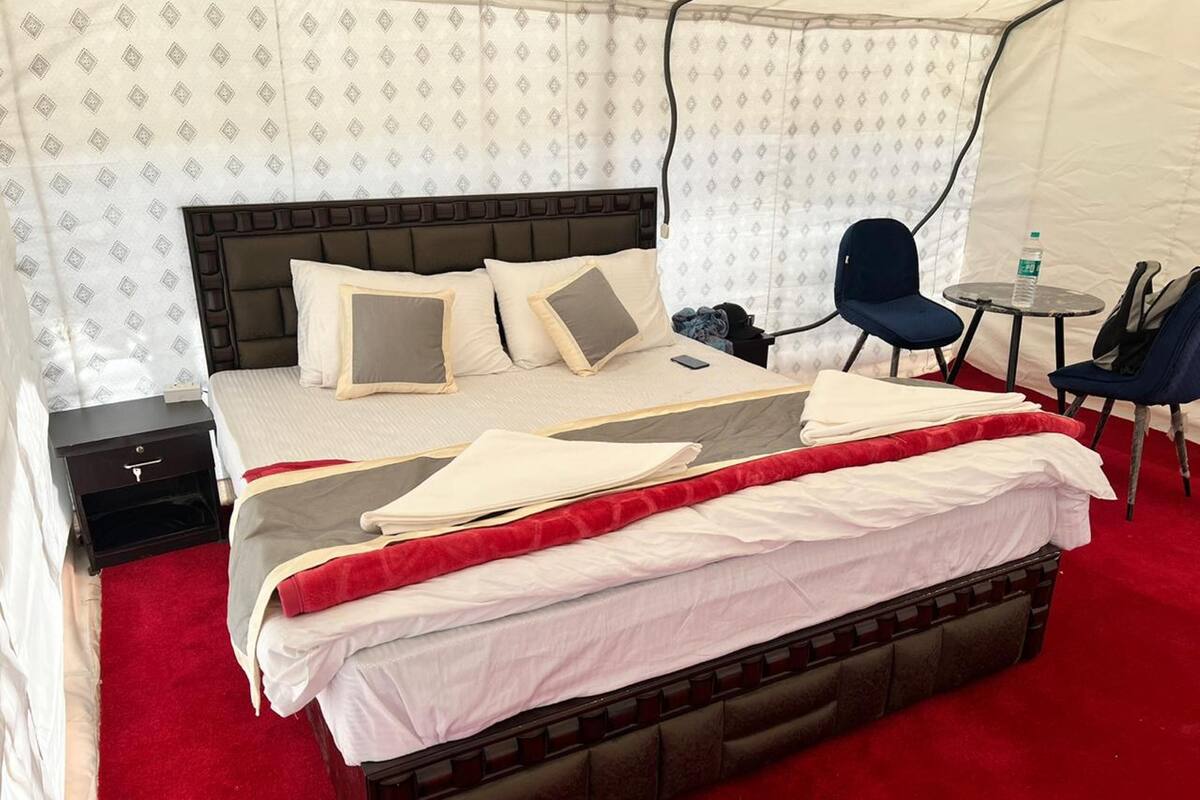 Une chambre d’hôtel avec un grand lit, une table de chevet, une chaise, une petite table et, au fond, une structure ressemblant à une tente.