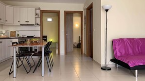 Eine moderne Küche mit weißen Schränken, einem Esstisch mit Stühlen, einem violetten Sofa und einer Stehlampe.