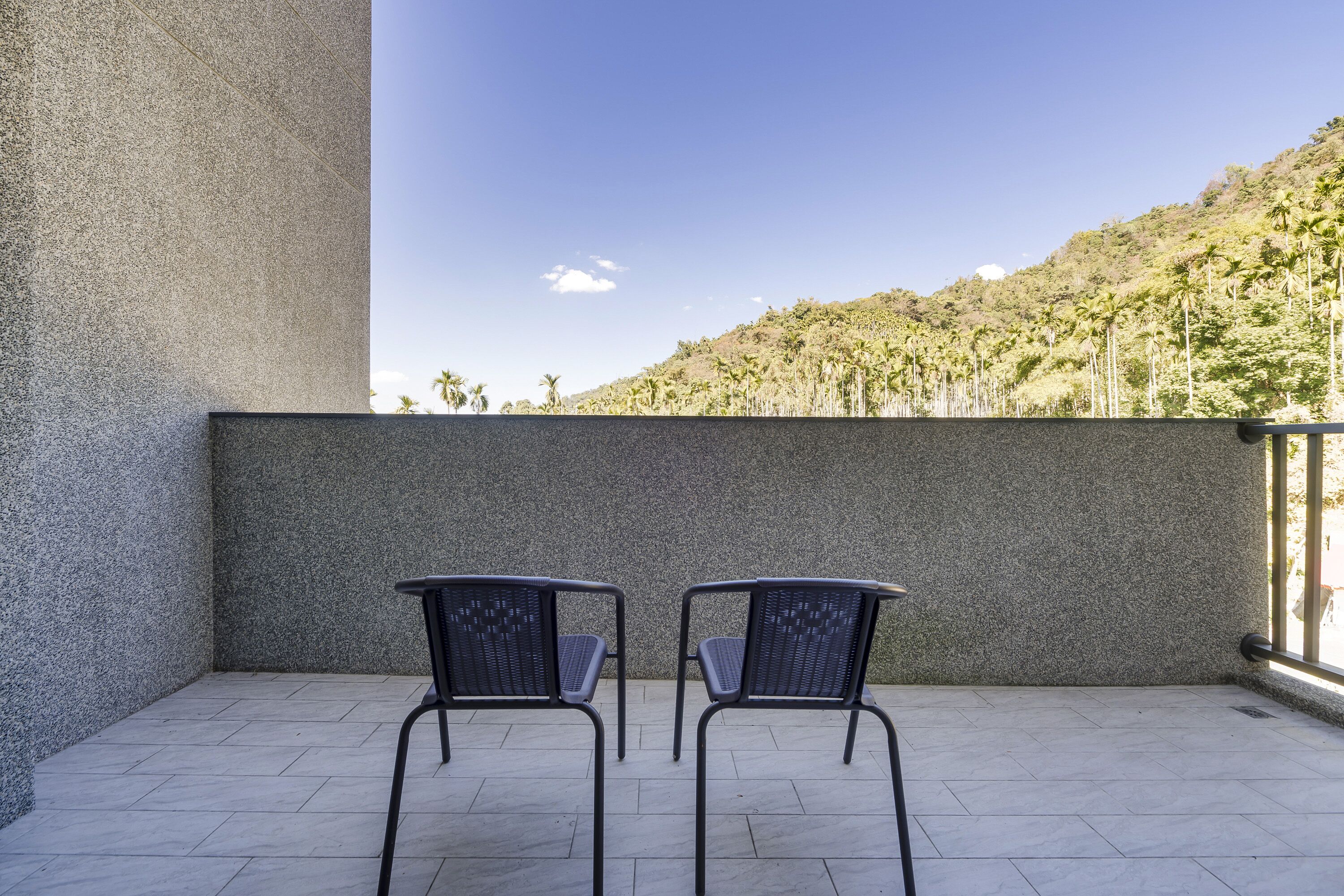 Un balcon avec deux chaises et une vue sur une colline parsemée de palmiers.
