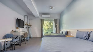 A modern hotel room with a desk, two beds, a large window with curtains, and an air conditioning unit. - Hills Valleys (Puli)