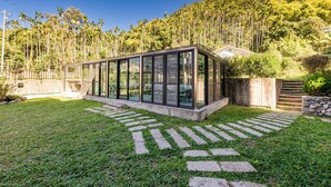 Una estructura moderna de cristal con un sendero de piedra que la conduce, rodeada de un césped cuidado y árboles altos.