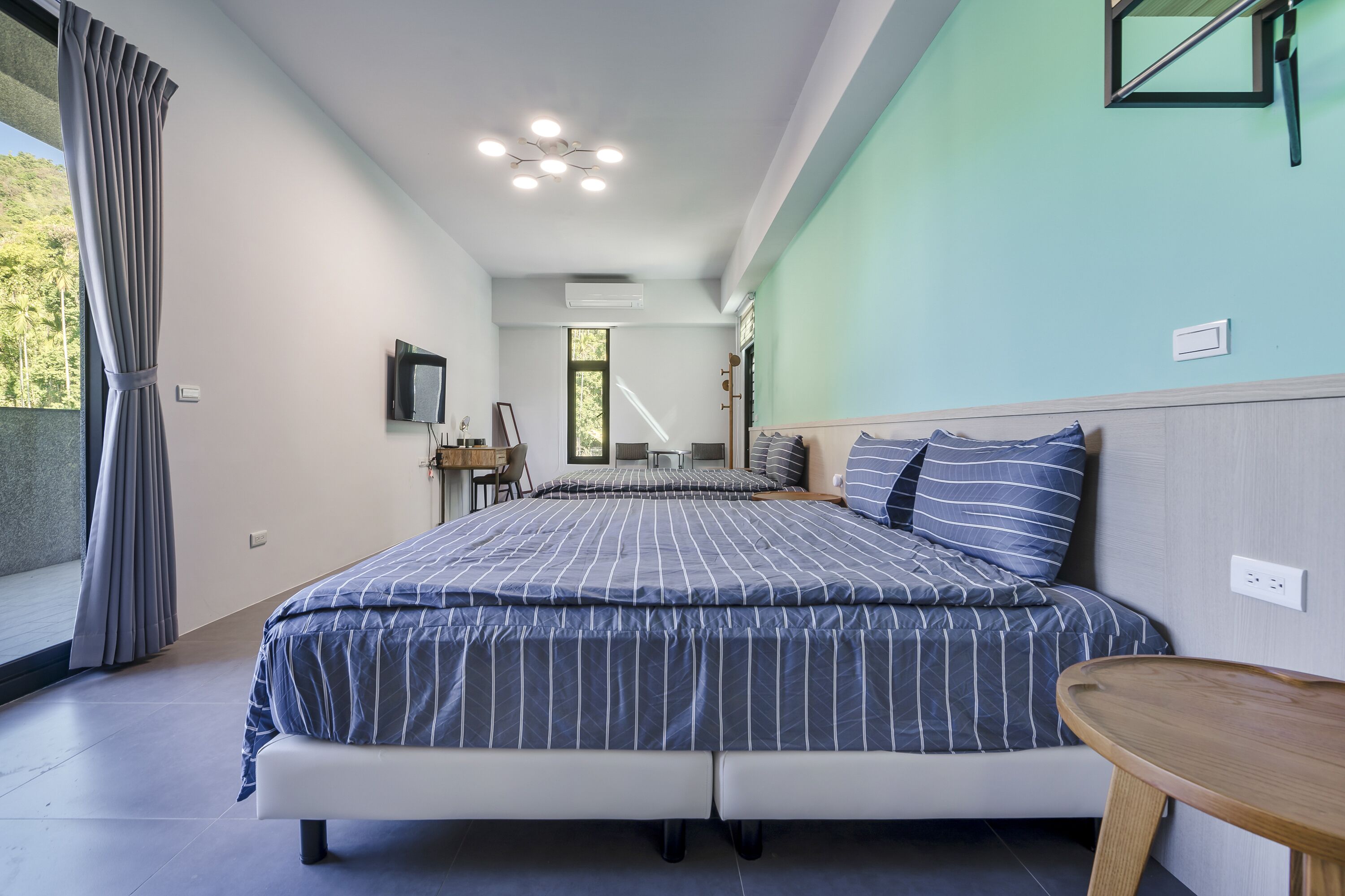 A modern bedroom with a large bed, a bedside table, a desk, and a chair.