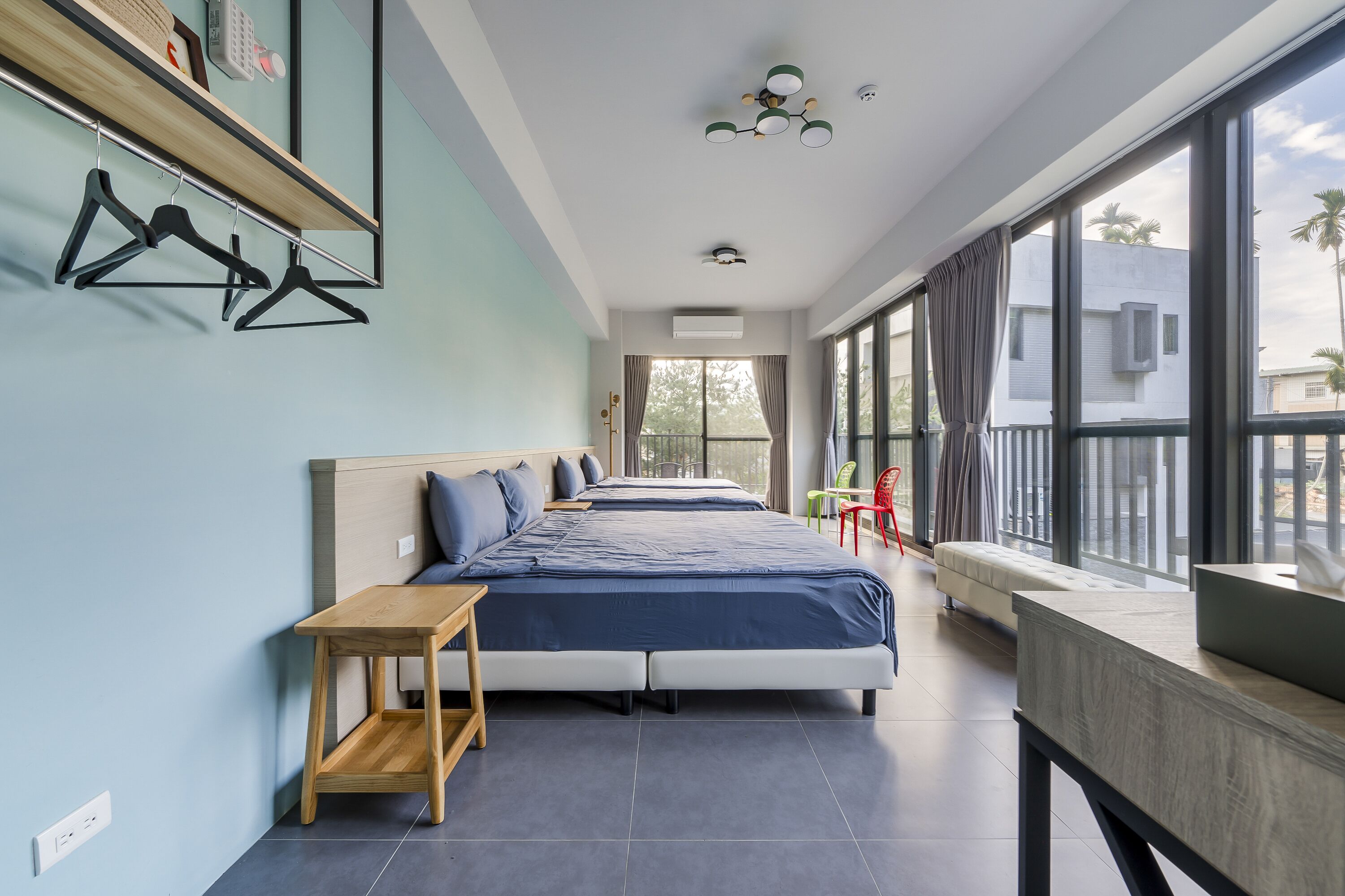 A modern hotel room with two beds, a wooden table, a balcony with a view, and a large window.