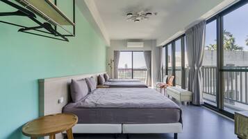 A modern hotel room with two beds, a small table, a chair, and large windows offering a view of the city.