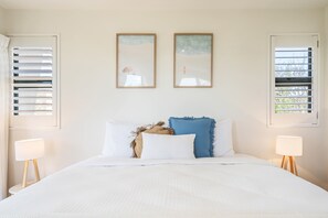 A bedroom with a bed, two wall-mounted picture frames, and two bedside lamps.