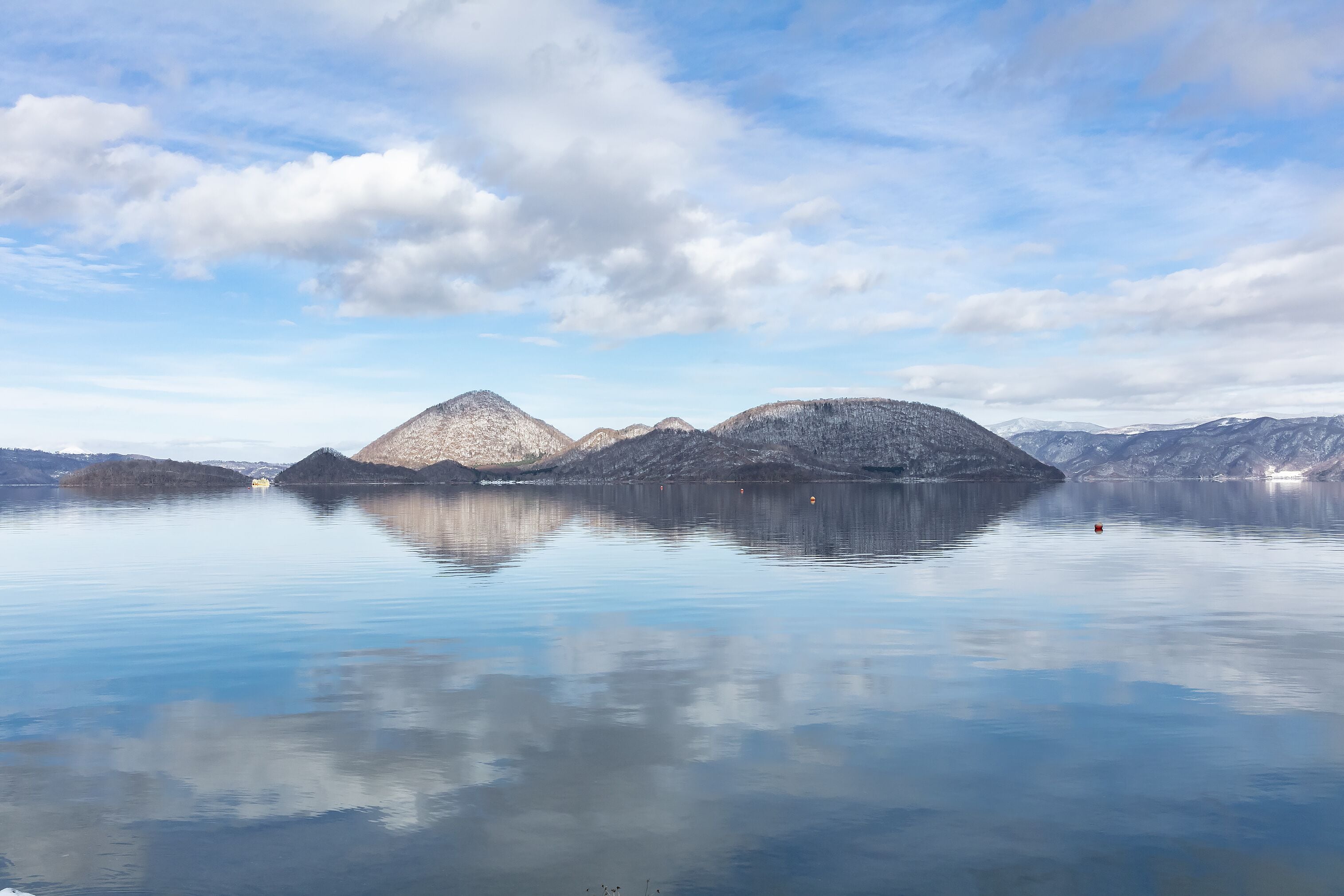 A calm lake with snow-capped mountains in the background and a clear sky.