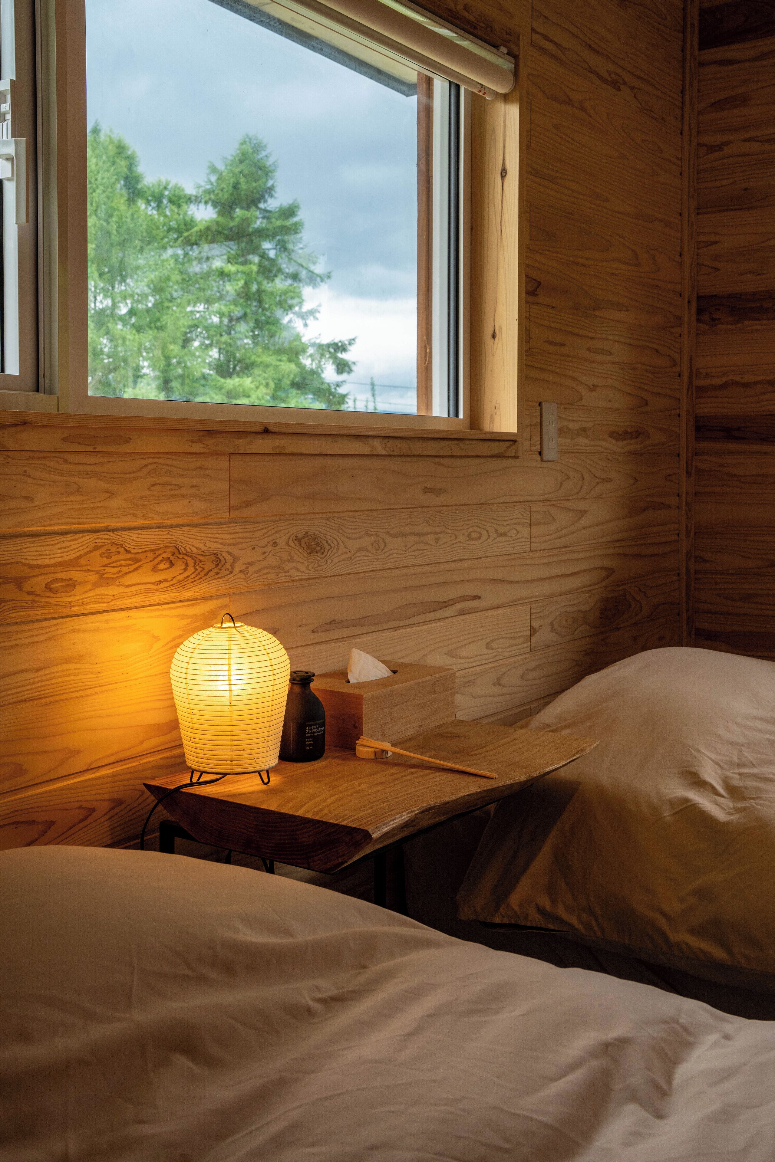 Une chambre dans un chalet en bois, avec une fenêtre, une table de chevet, une lampe et deux lits.