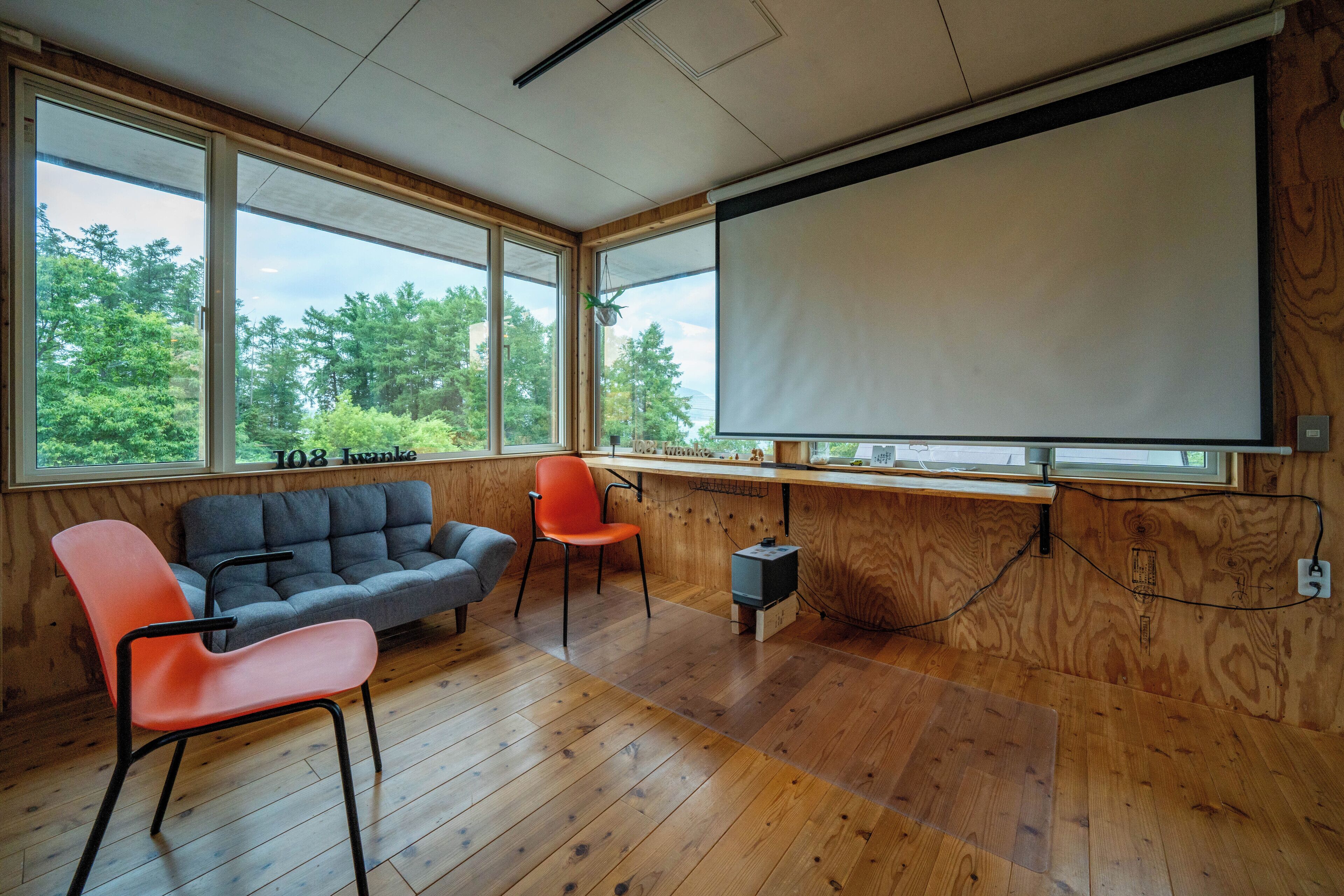 Une pièce avec un plancher en bois, un canapé gris, un fauteuil orange et un grand écran de projection.