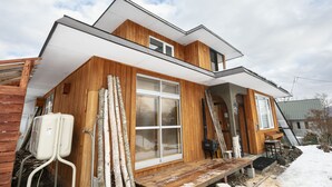 Una moderna casa in legno con un'ampia finestra, un terrazzo in legno e un camino.