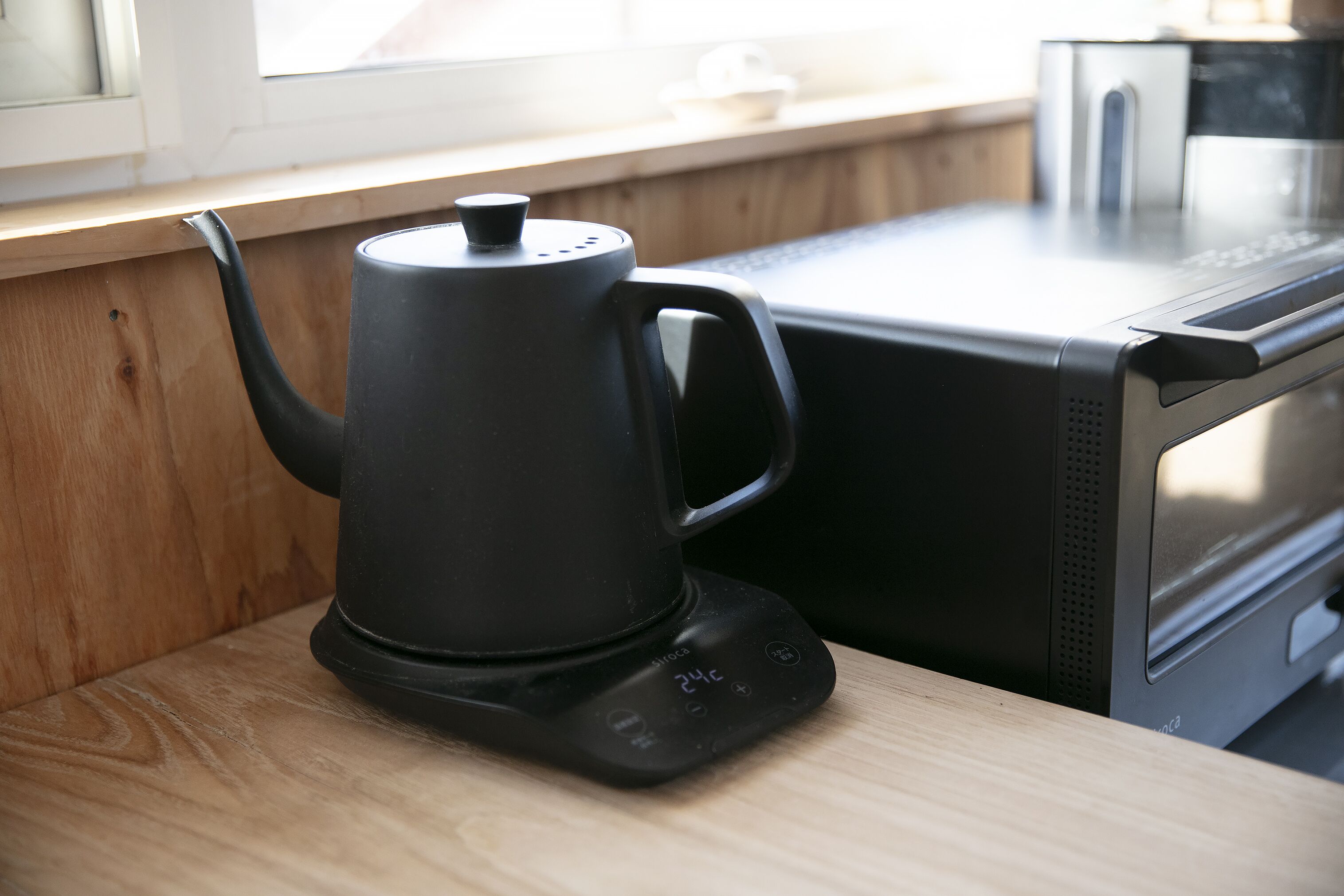 A black electric kettle on a wooden countertop next to a microwave.