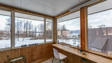 Une pièce dotée de grandes fenêtres, d’un bureau en bois et d’une chaise blanche.