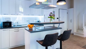A modern kitchen with white cabinets, a built-in microwave, a coffee maker, and a small island with two chairs and a vase of flowers. - Bonne Chance Apartments (Zagreb)