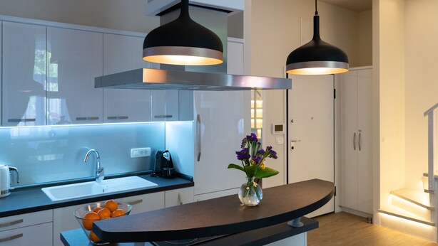 A modern kitchen with white cabinets, a black countertop, and two pendant lights. - Bonne Chance Apartments (Zagreb)