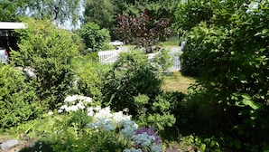 Ein Garten mit verschiedenen Pflanzen und Blumen, ein weißer Zaun und ein geparktes Auto.