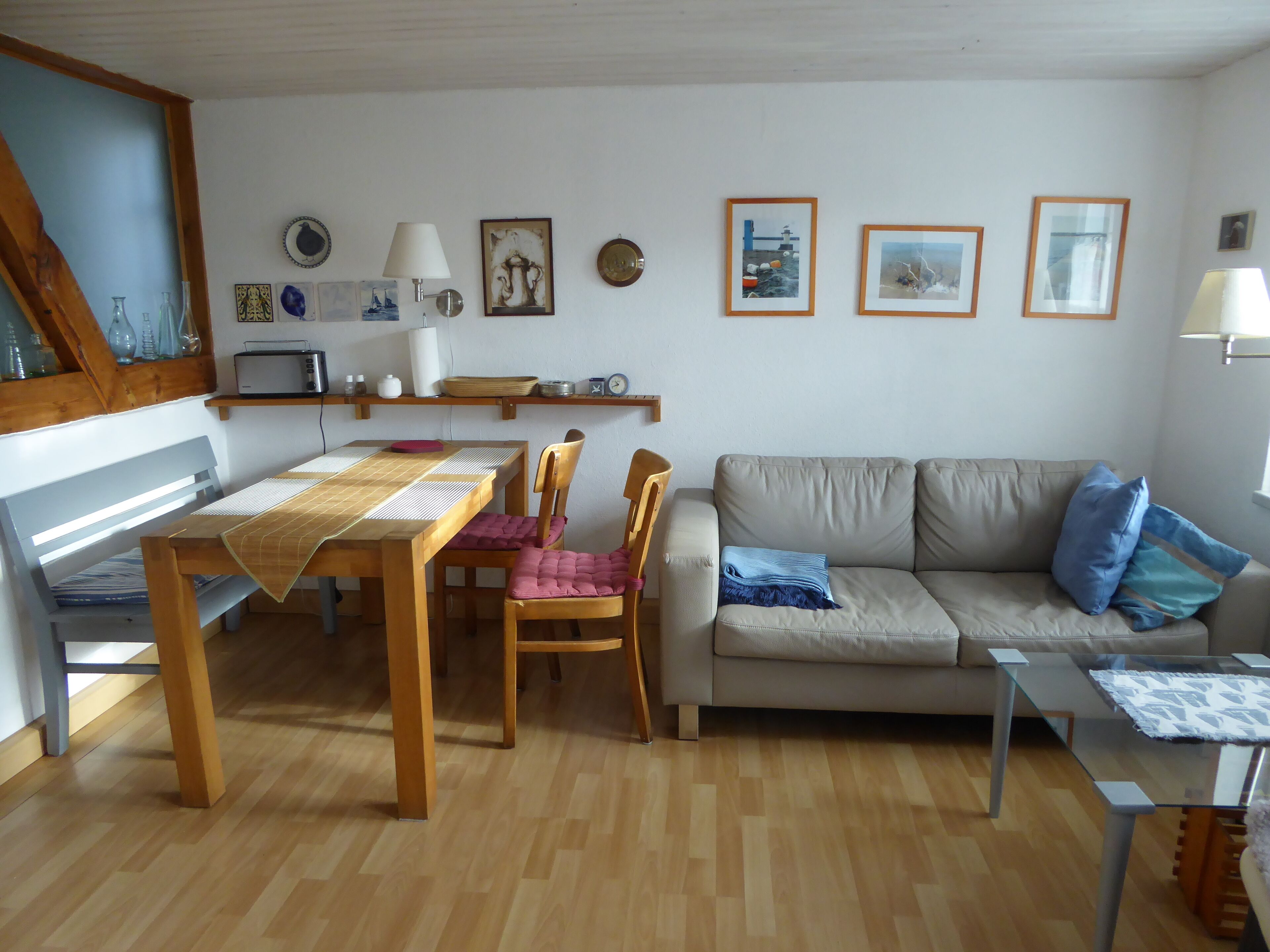Ett vardagsrum med ett matbord i trä, stolar, en soffa och ett soffbord i glas.