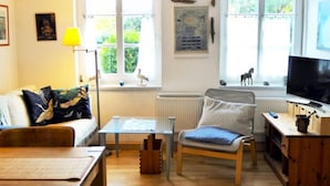 Ein gemütliches Wohnzimmer mit einer Couch, einem kleinen Tisch, einem Sessel und einem Fernseher.