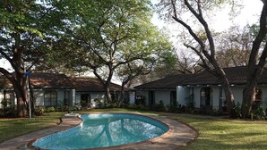 A swimming pool surrounded by a stone deck, with a grassy lawn and trees in the background. - Zimbara (Victoria Falls)