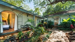 A cozy, well-maintained garden with a stone pathway leading to a building with an open porch and a dining area. - Zimbara (Victoria Falls)