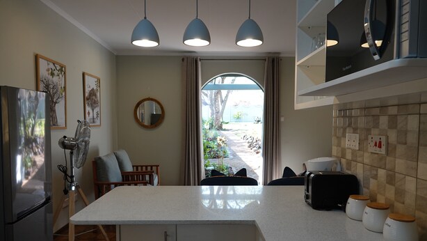 A modern kitchen with a central island, a refrigerator, a coffee maker, and a toaster. There is a dining area with a chair and a table. - Zimbara (Victoria Falls)