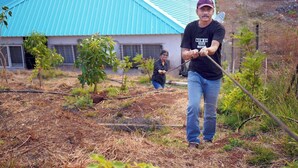 A man in a black t-shirt and jeans holding a rope, standing in a garden with a house in the background. - The Serenity Resort (Mahabaleshwar)