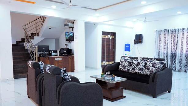 A modern hotel lobby with a reception desk, a sofa set, a coffee table, and a staircase leading to an upper floor. - The Serenity Resort (Mahabaleshwar)