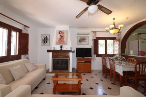 Una sala de estar con sofá, mesa de centro, chimenea, televisor, mesa de comedor, sillas y obras de arte en las paredes.