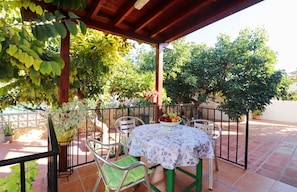 Un patio cubierto con una mesa lista para comer, rodeado de sillas y macetas con plantas.
