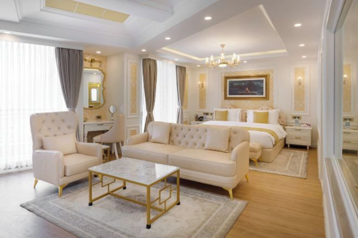 A hotel room with a bed, two sofas, a coffee table, a desk, and a large window.