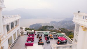 A rooftop terrace with outdoor seating, overlooking a valley and a body of water. - Pokhara Panorama Resort and Spa-Luxury Redefined (Pokhara)