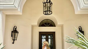 A person standing in a doorway with a suitcase, a potted plant, and a wall-mounted light fixture. - Las Palmas  | Minutes to TPC | Tranquil Hacienda (Scottsdale)