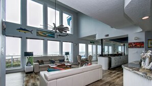 A spacious living room with large windows, a ceiling fan, and a view of the ocean. - Beachfront 4BR/4.5BA Luxury Getaway! (Galveston)