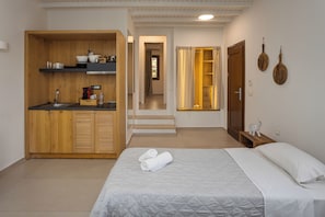 Habitación de hotel compacta con kitchenette, cama con cubrecama acolchado y baño pequeño con ducha.
