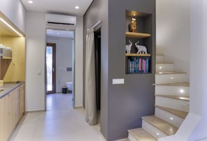 Un interior moderno con una escalera, una estantería con objetos decorativos y una zona de cocina.