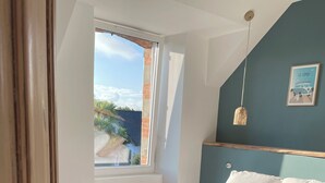A bedroom with a large bed, wooden flooring, a window with a view, and a blue accent wall. - Maison des Années 30 Avec spa (Plounéour-Brignogan-plages)