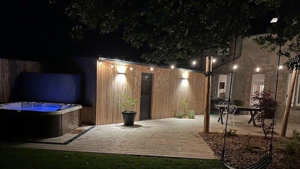 A backyard with a hot tub, wooden deck, potted plants, and a swing. - Maison des Années 30 Avec spa (Plounéour-Brignogan-plages)