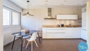 A modern kitchen with white cabinets, a wooden countertop, and a hanging light fixture. - Le Sainte Anne- appartement avec vue Lac. (Annecy-le-Vieux)