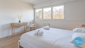 A bedroom with a large bed, a bedside table, a chair, and a window. - Le Sainte Anne- appartement avec vue Lac. (Annecy-le-Vieux)