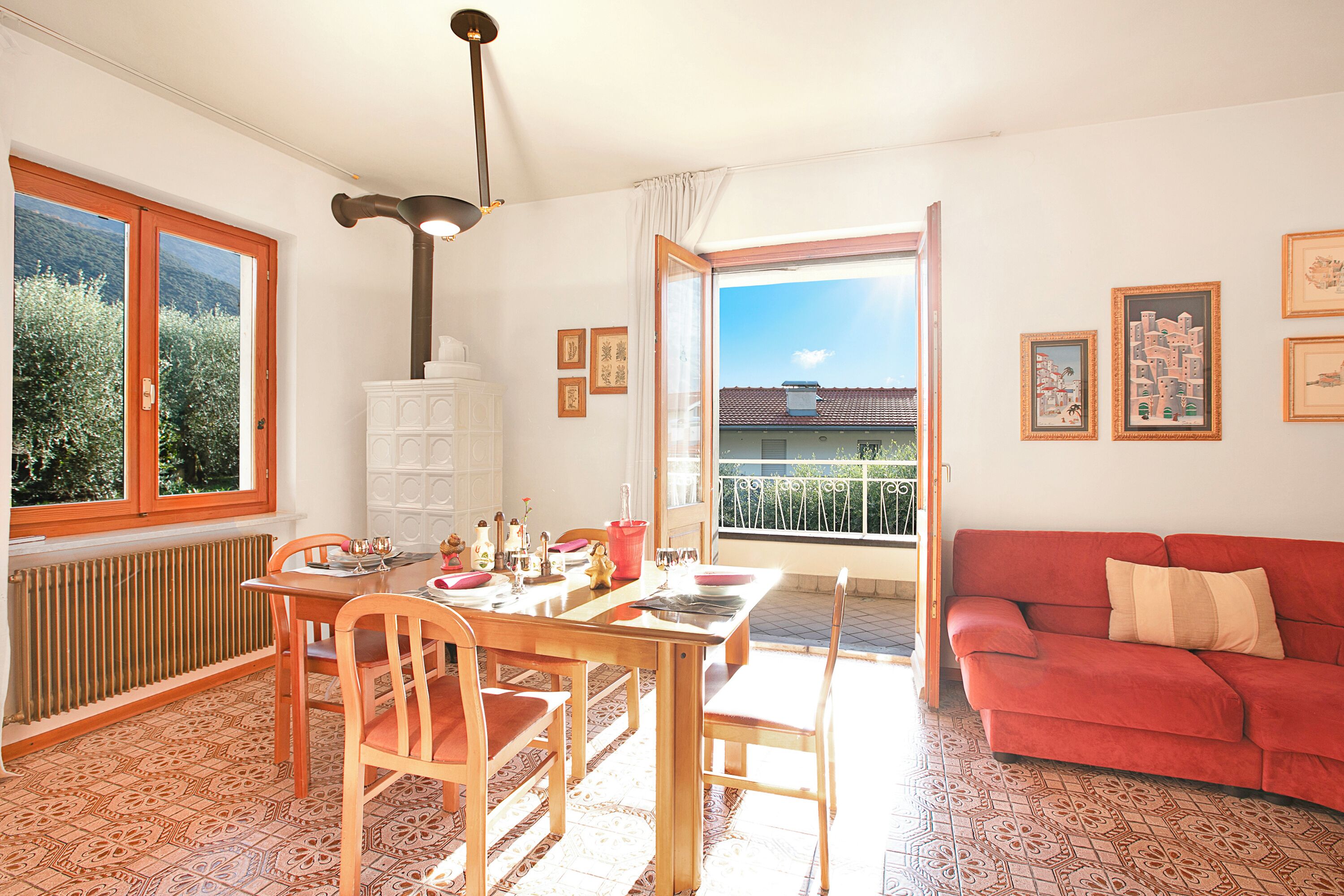 Un coin repas avec une table dressée pour quatre personnes, un canapé rouge et un balcon offrant une vue sur les bâtiments.