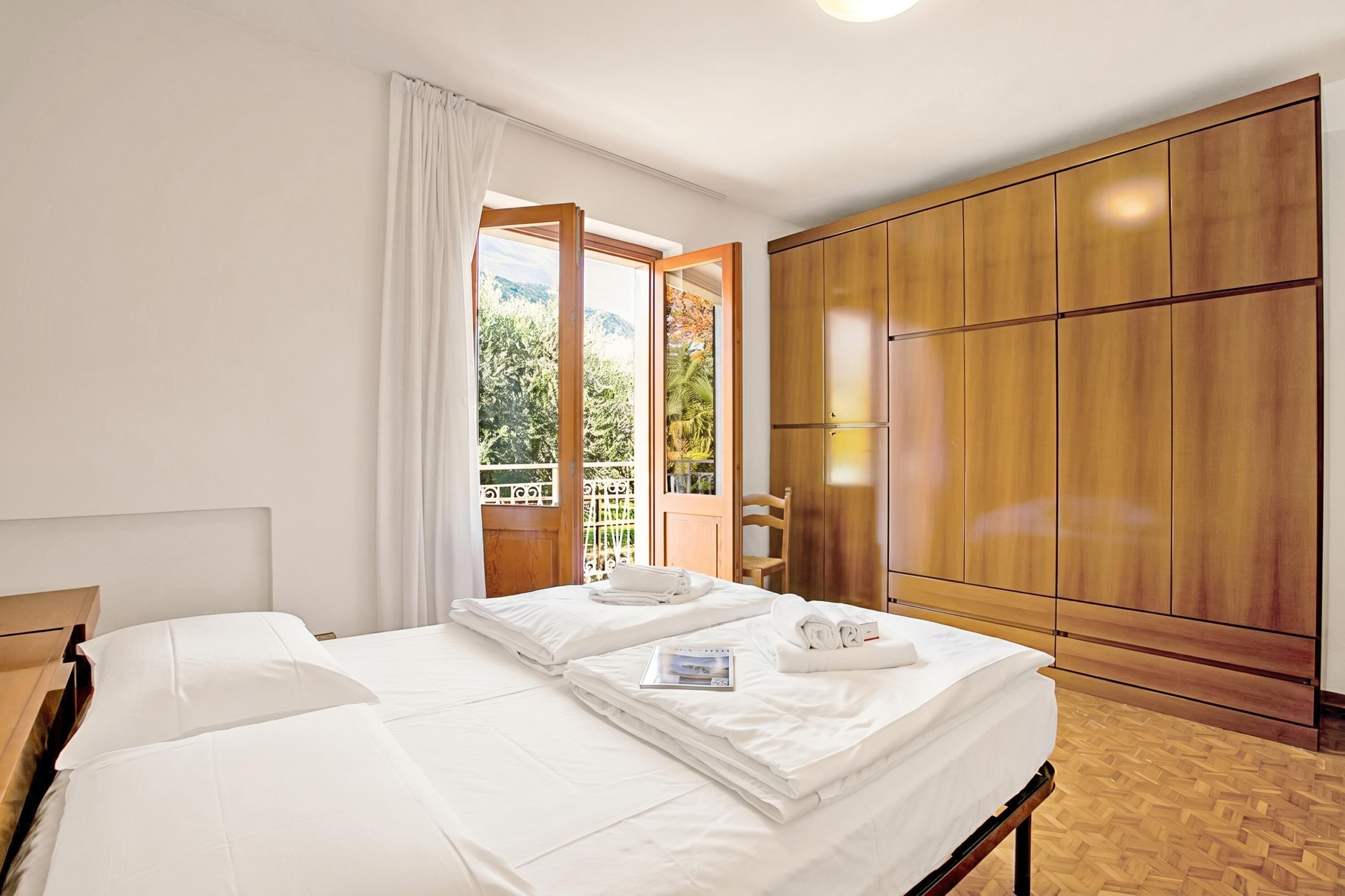 A hotel room with a bed, wooden wardrobe, and a balcony with a view.