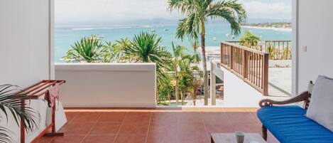A balcony with a view of the ocean, a wooden bench, a blue sofa, and a small table with a book and a cup.