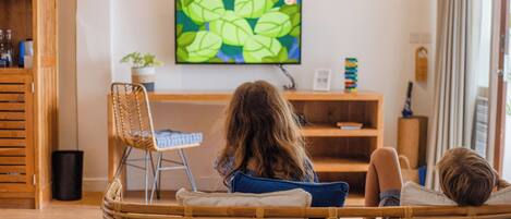 Una habitación con una televisión en la pared, una silla de mimbre, una cama y una mesita con una planta.
