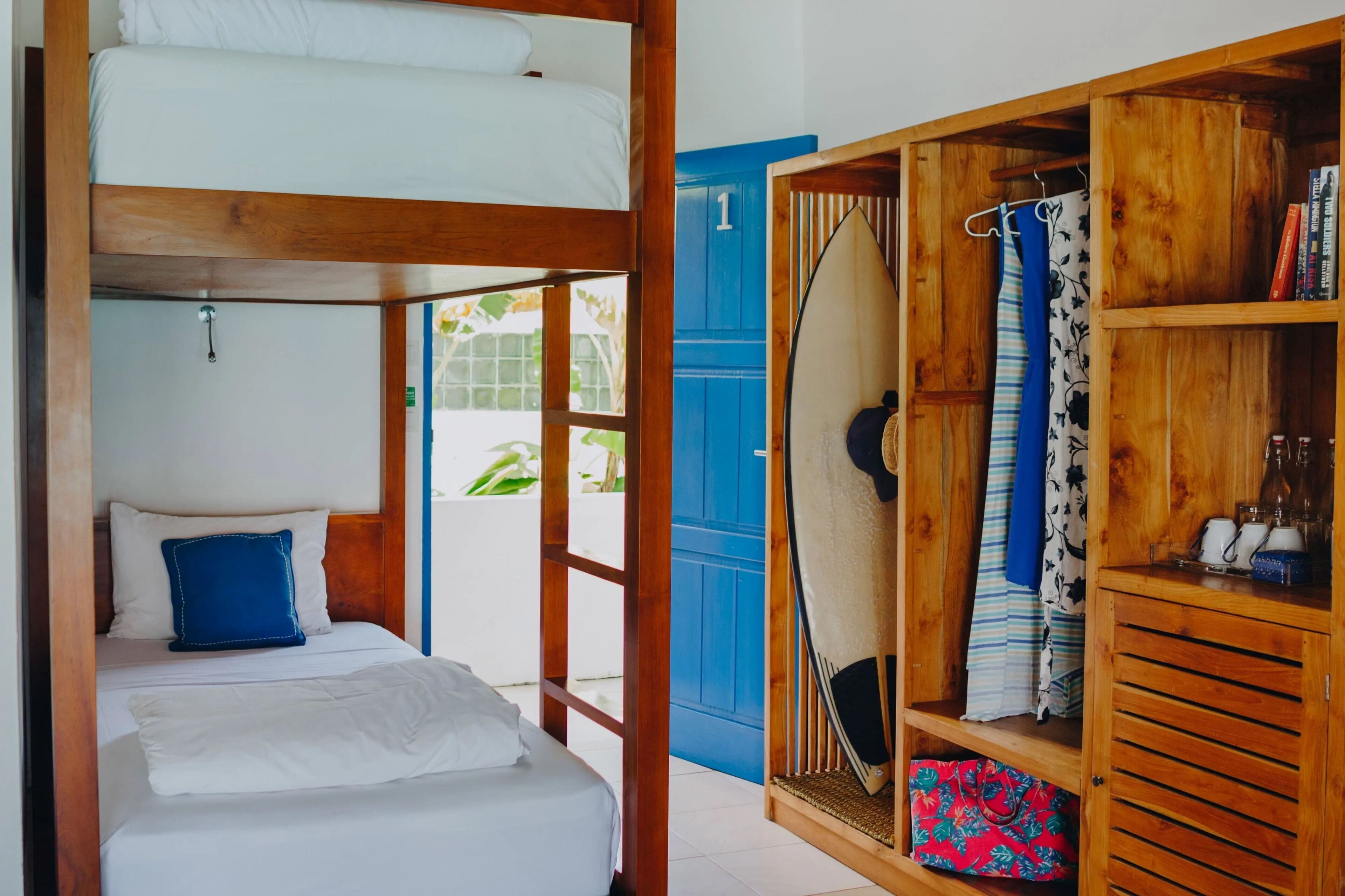 Een kamer met een stapelbed, een houten garderobe en een blauwe deur.