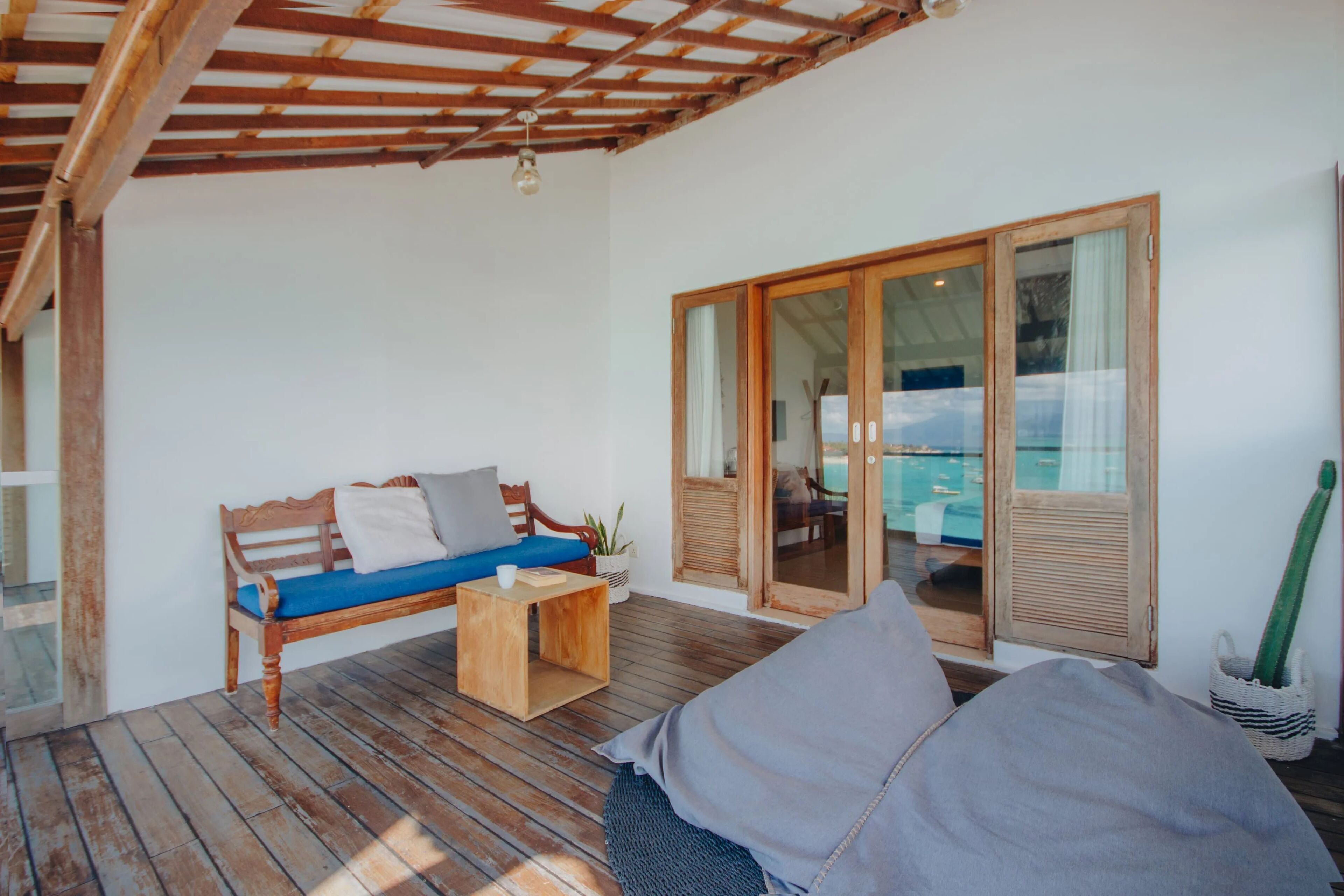 A wooden deck with a bench and a table, a sliding glass door leading to a pool area, and a cactus plant.