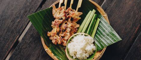 A meal of grilled skewers, rice, and cucumber slices on a wooden table.