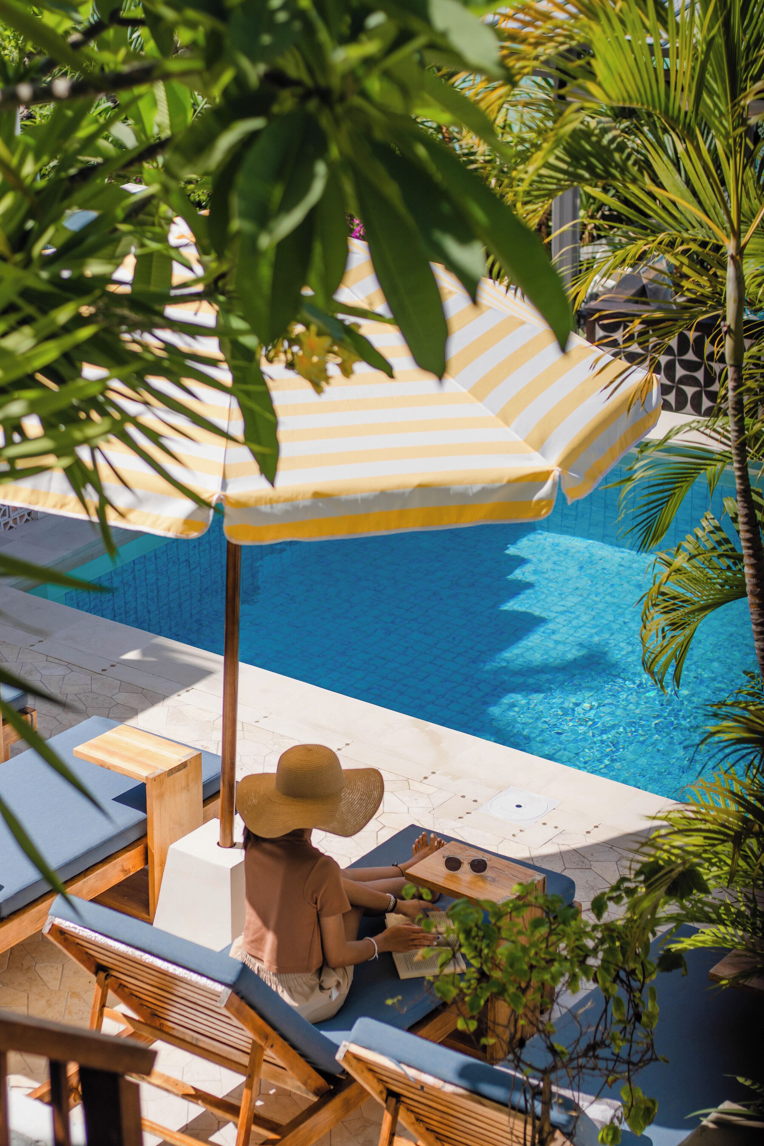 A poolside area with lounge chairs, a striped umbrella, and a person relaxing.