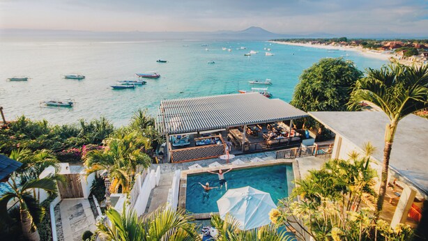 Un resort con piscina, mobiliario exterior y barcos en el agua.